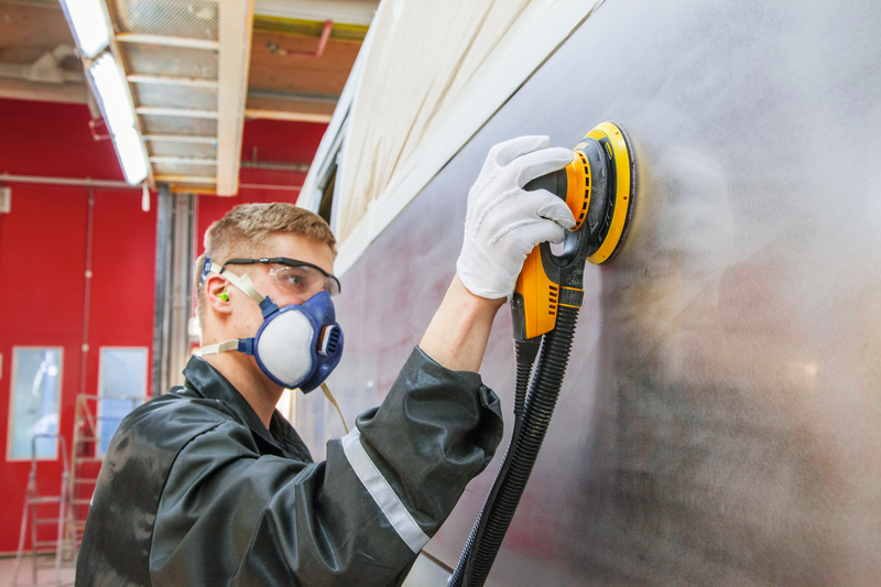 Mann mit Halbmaske bedient eine gelbe Druckluft Schleifmaschine und schleift eine Wand